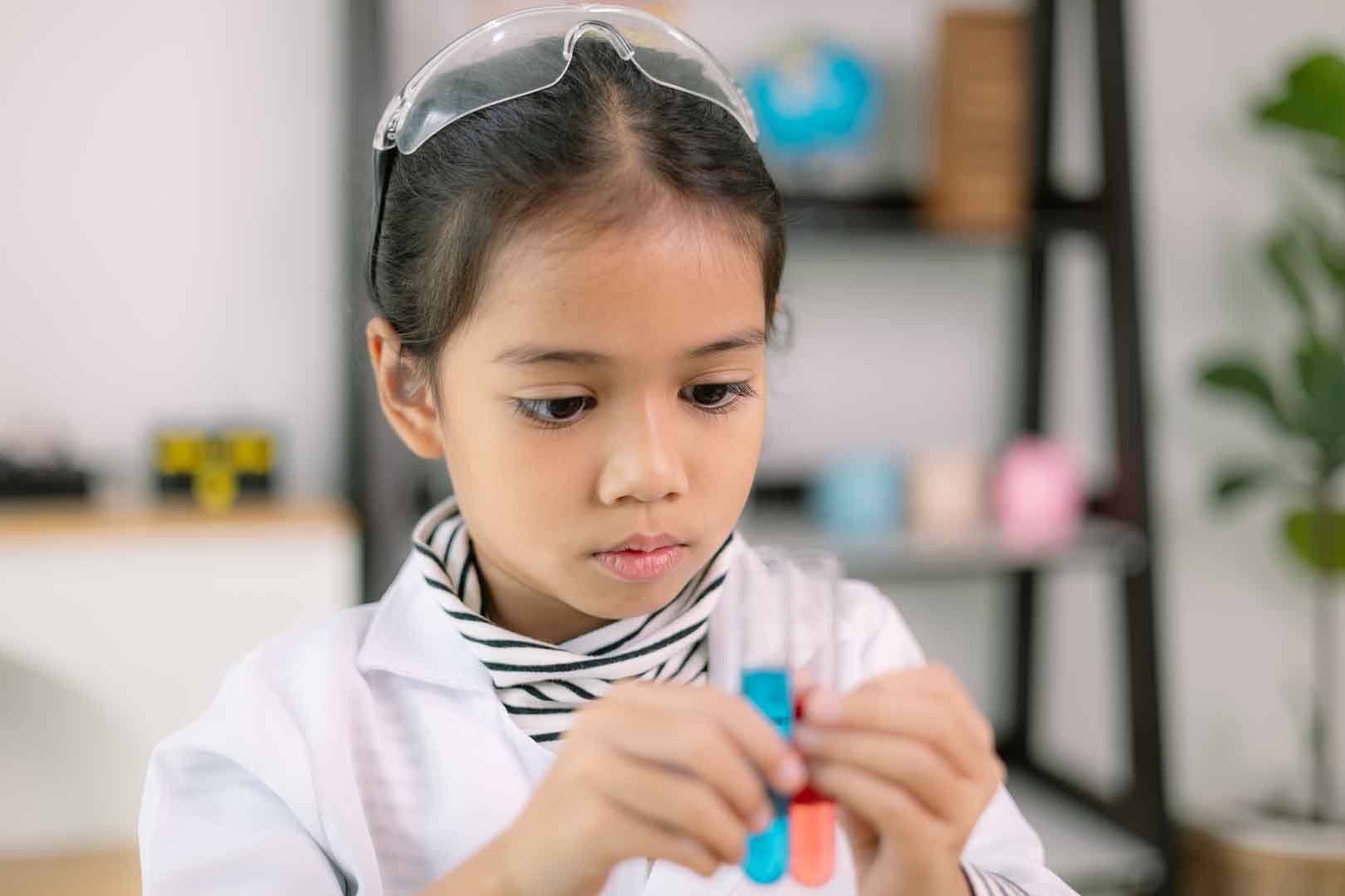 A young girl in a lab coat concentrating on mixing colors in test tubes, demonstrating focus and executive functioning during a hands-on learning activity.