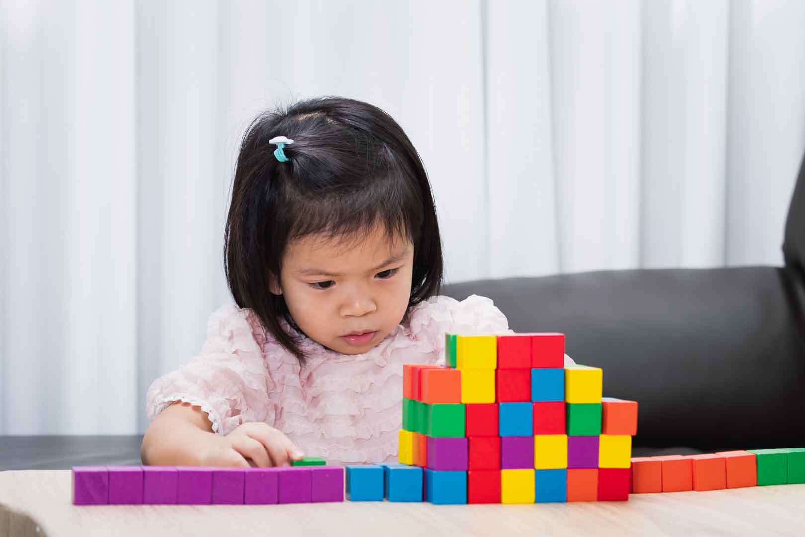 A young girl focused on building with colorful blocks during a developmental play-based occupational therapy session.