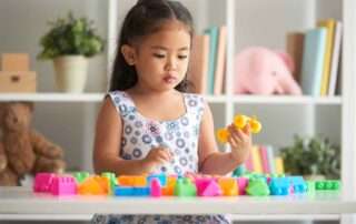 Young girl playing with colorful blocks to build cognitive and motor skills, highlighting the importance of play at OrbRom Center Phnom Penh.