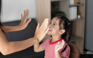 Child smiling while receiving a high-five during speech therapy session at OrbRom Center in Phnom Penh