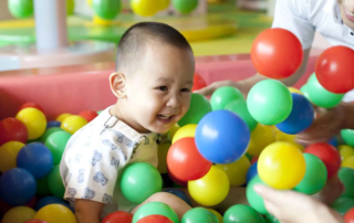 Young child smiling and playing in a colorful ball pit during a sensory integration occupational therapy session at OrbRom Center in Phnom Penh