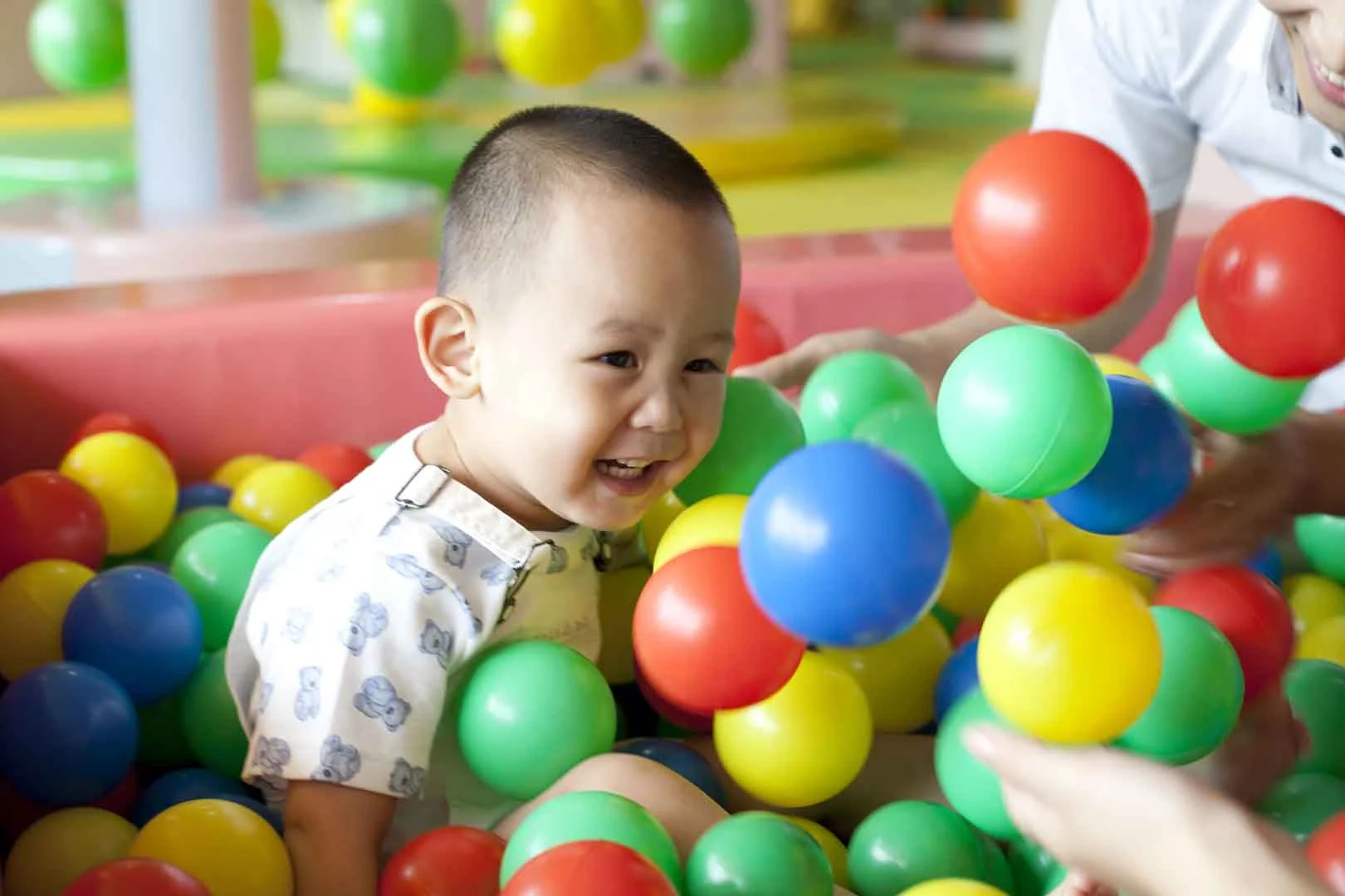 Young child smiling and playing in a colorful ball pit during a sensory integration occupational therapy session at OrbRom Center in Phnom Penh