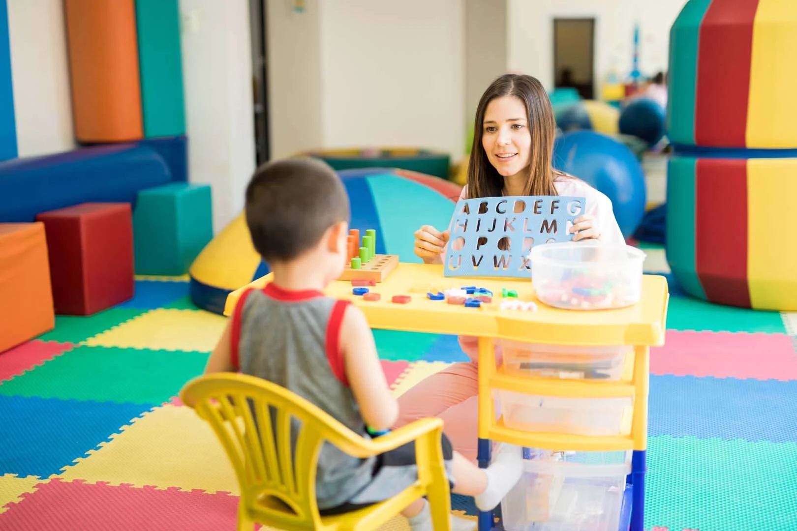 Therapist using alphabet stencil and play tools with child in colorful occupational therapy room in Phnom Penh