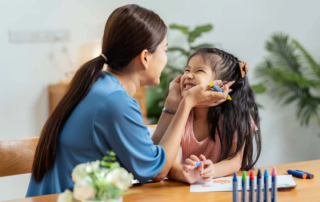 A speech therapist warmly interacts with a smiling girl during a playful therapy session at OrbRom Center in Phnom Penh, Cambodia.