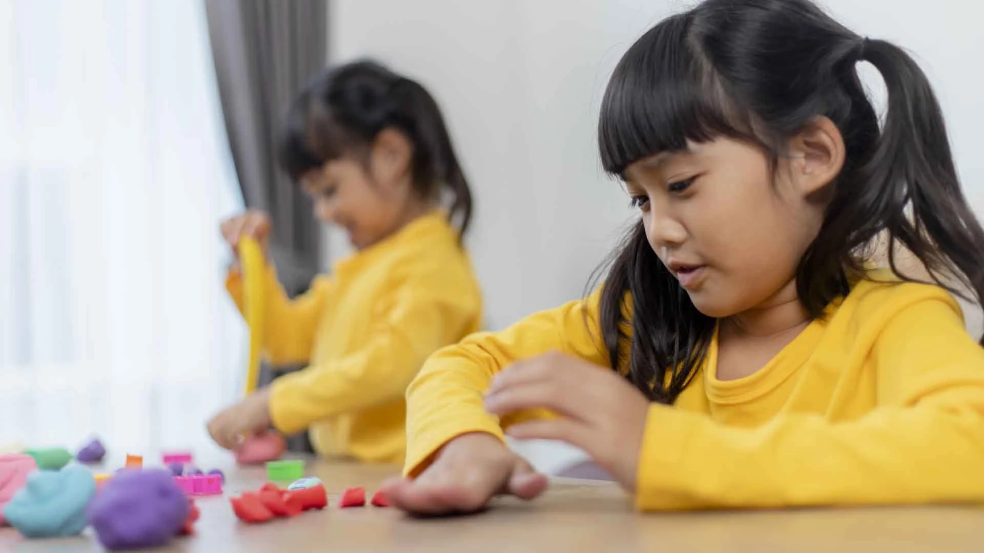 Two young girls in Phnom Penh development school playing with colorful dough to support sensory and fine motor development