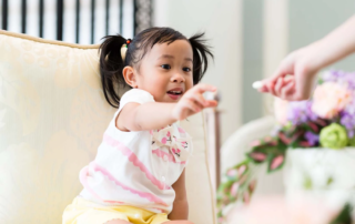 A young girl reaching for an item being offered—demonstrating an early communication skill known as requesting in speech development.