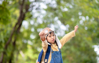 A confident young girl dressed as a pilot pretends to fly, symbolizing imaginative play used in speech therapy sessions in Phnom Penh.
