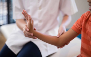 A therapist supporting a child’s arm during a physical rehabilitation session focused on improving motor control and strength