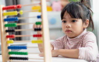 Young girl concentrating on abacus counting activity, showing early signs of potential learning challenges