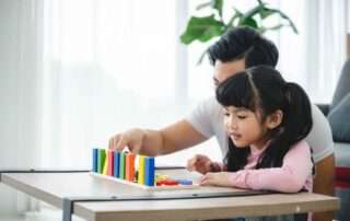 Father supporting young girl as she plays with colorful educational blocks, part of early developmental learning activities