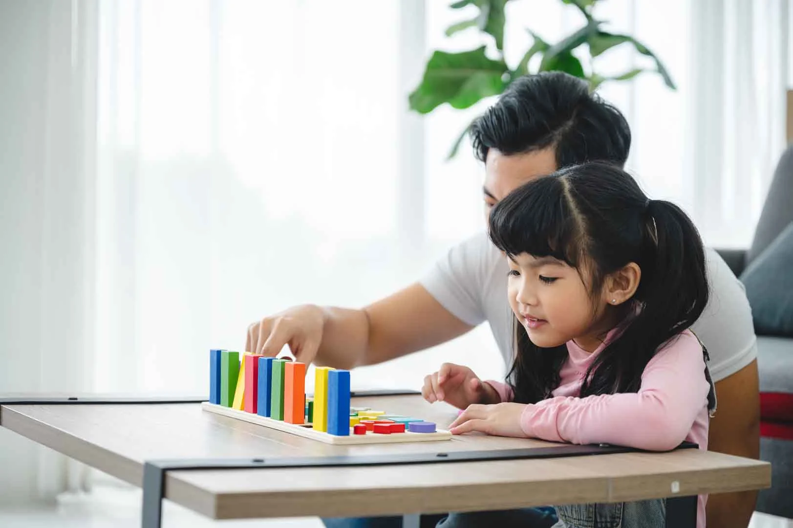 Father supporting young girl as she plays with colorful educational blocks, part of early developmental learning activities