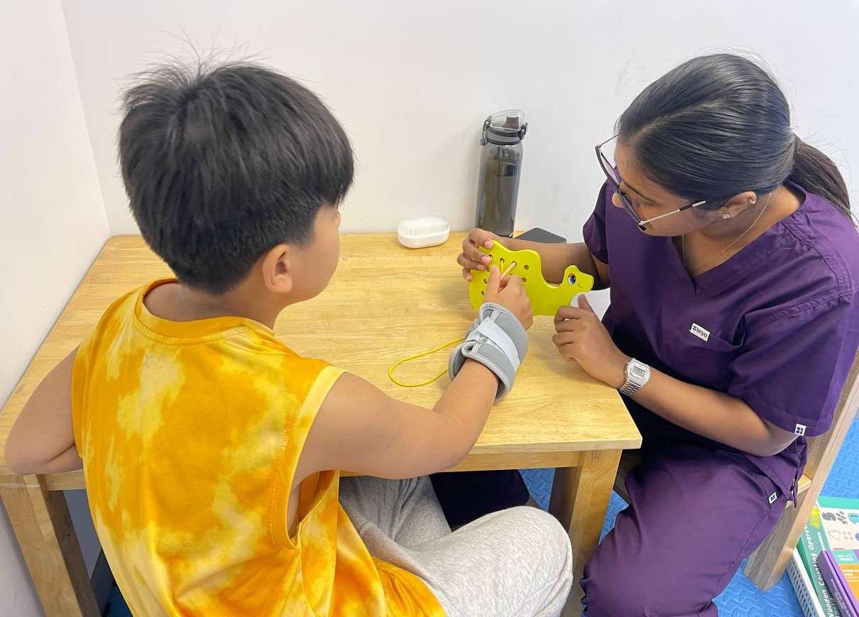 Child and occupational therapist at OrbRom Center using threading activity to improve fine motor skills