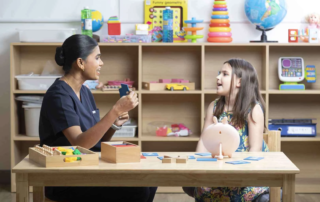 A therapist supports a preschool girl during a speech therapy session using Montessori-inspired learning cards at OrbRom Center.