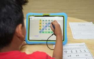 Child practicing digraphs on a tablet with instructor guidance during a structured phonics intervention session.