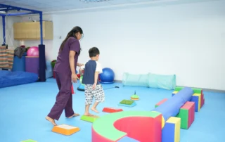 Occupational therapist guiding a child through balance and motor-planning activities in a sensory gym at OrbRom Center