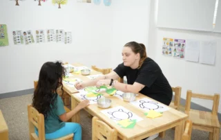 Teacher supporting a child during a hands-on fine motor activity at a preschool table