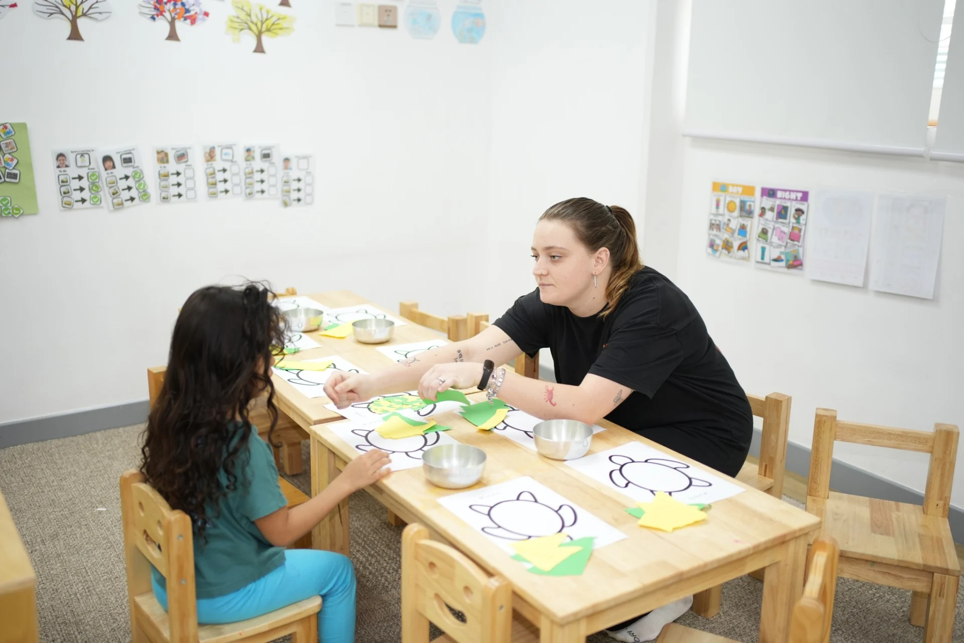 Teacher supporting a child during a hands-on fine motor activity at a preschool table