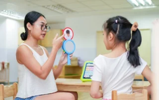 Speech therapist using AAC tools, emotion cards, and a mirror to teach communication and emotional recognition during a one-on-one therapy session at OrbRom Center.